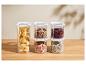 Récipients de rangement transparents avec pâtes, lentilles, haricots, muesli et riz sur un comptoir en bois.