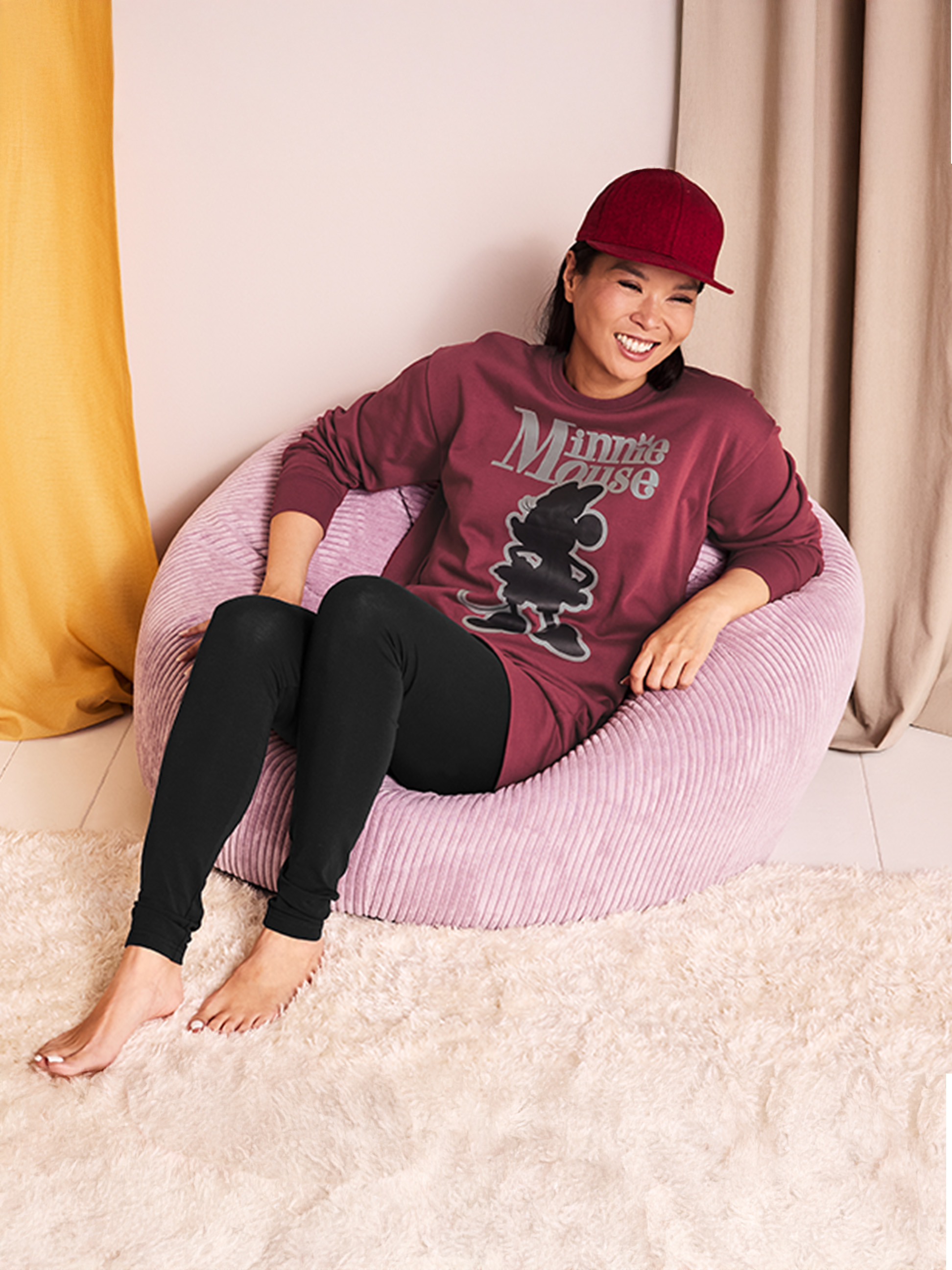Femme en pyjama Minnie Mouse et casquette assise dans un pouf rose.
