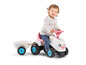 Een kind rijdt op een roze Falk tractor met aanhanger.