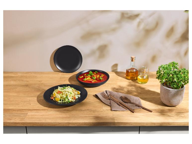 Assiettes de pâtes et de soupe dans des bols noirs, avec des couverts en cuivre et de l'huile sur une table en bois.