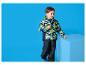 Jongen in kleurrijke camouflagejas en donkere broek bij een blauwe kubus.