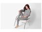 Vrouw in grijs gebreid loungewear zit op een stoel.