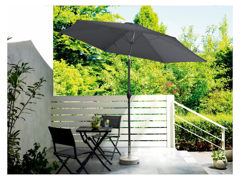 Een grijze parasol met een stenen voet, een zwarte tafel en stoelen op een patio