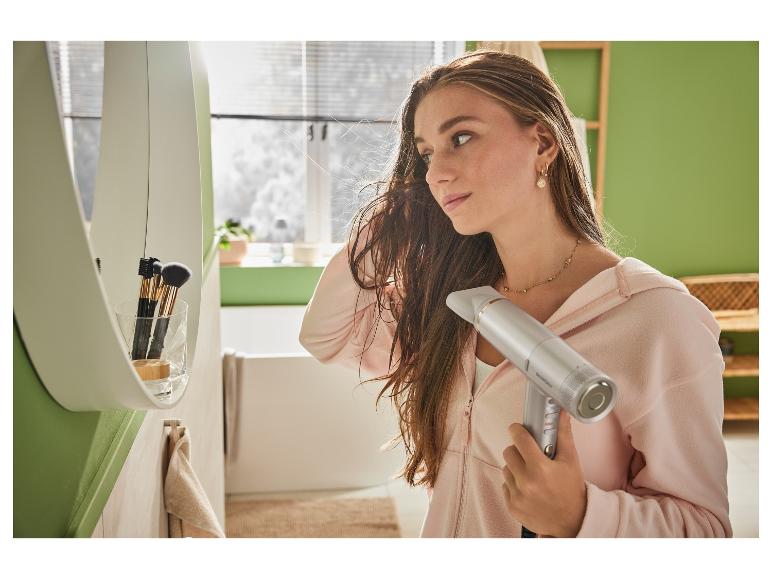 Une femme sèche ses cheveux avec un sèche-cheveux SensCare dans la salle de bain.