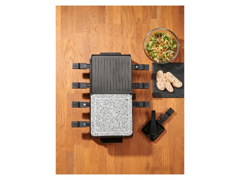 Raclette grill met salade en brood op een houten tafel.