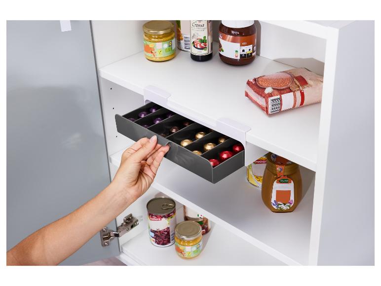 Une main tire un tiroir à capsules d'une armoire de cuisine.