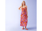Een vrouw draagt een roze maxi-jurk met bloemenprint en rode sandalen.