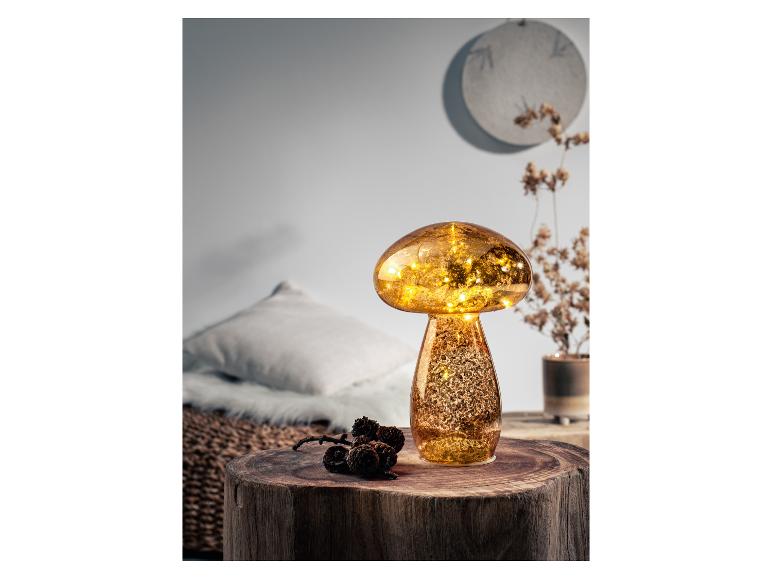 Verlichte decoratieve paddenstoelvormige lamp met gouden effect, op een houten tafeltje.