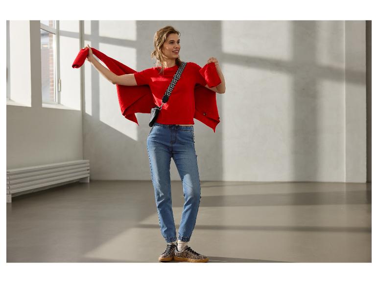 Lachende vrouw in rode trui, rood vest, jeans en sneakers met luipaardprint.
