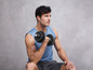 Man in blauwe tanktop die een halter met gewichten vasthoudt.