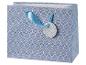 Sac cadeau bleu avec un motif de feuilles blanches et une étiquette ronde à motif de carrés.