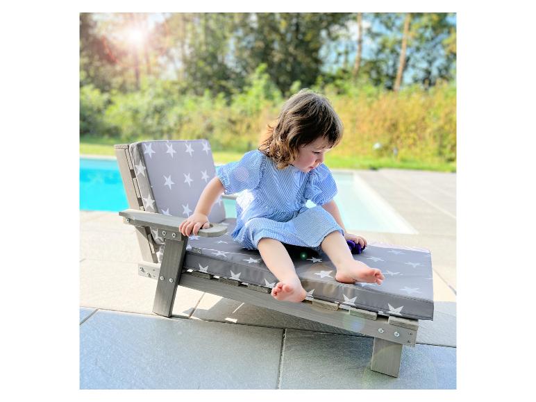 Jeune enfant sur une chaise longue en bois avec des coussins gris à étoiles blanches près d'une piscine.