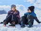 Twee kinderen dragen winterkleding en zitten in de sneeuw.