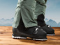 Zwarte ski-laarzen met groene broek op een houten vloer.