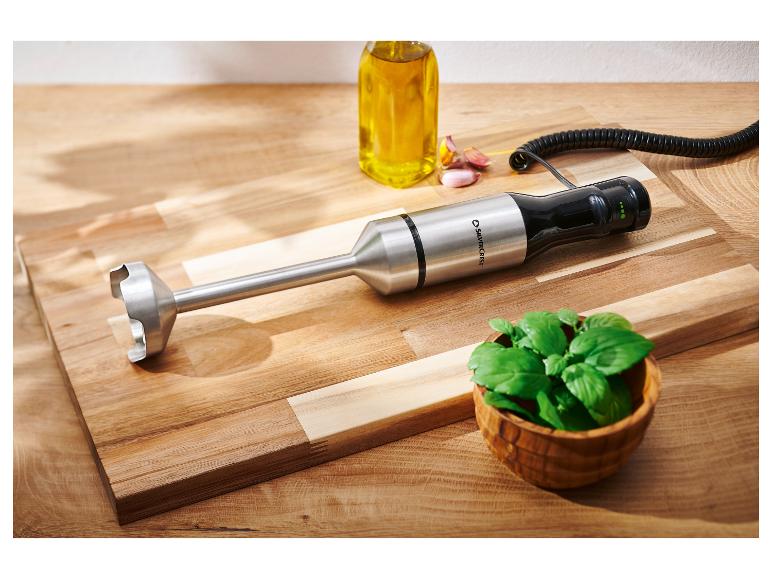 Mixeur plongeant, bouteille d'huile, ail et basilic sur une planche en bois.