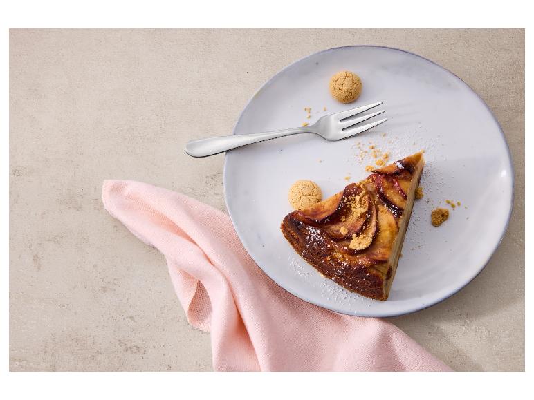 Een stuk appeltaart met vork en koekjes op een bord, op een roze servet.