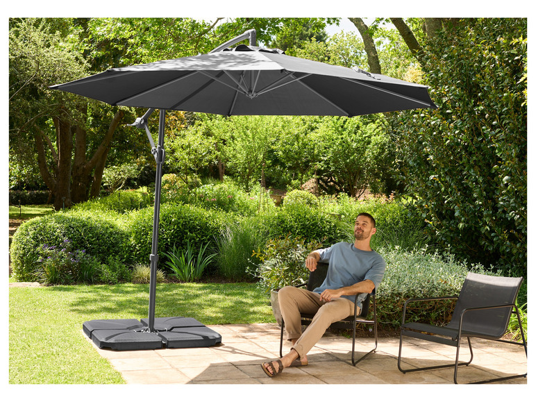 Een grijze parasol met een vierkant voetstuk in een tuin met een man op een stoel