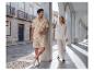 Homme en ensemble chemise et short à motifs de feuilles, femme en chemise et pantalon blancs, dans une rue à arcades.