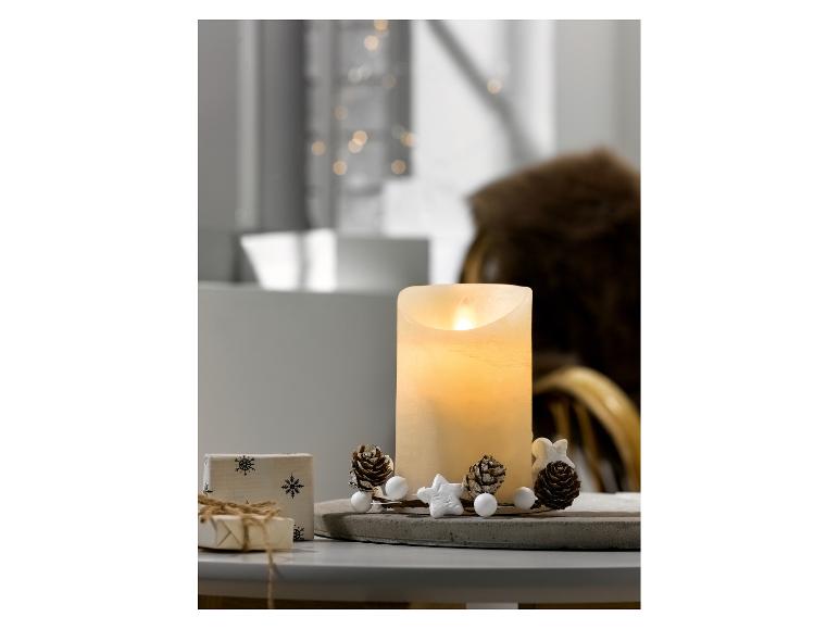 Decoratieve kaars met kerstornamenten en cadeaus op een tafel.