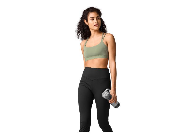 Vrouw in groene sportbeha en zwarte legging met een waterfles.