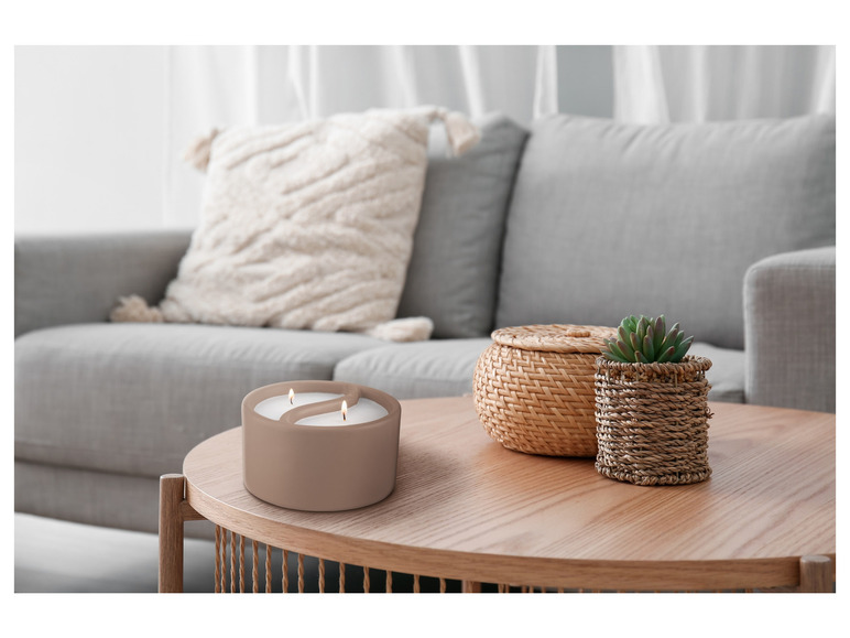 Une bougie parfumée ou décorative allumée sur une table basse avec un panier et une plante.