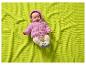 Bébé en pull à capuche rose et pantalon beige sur une couverture gaufrée vert lime.
