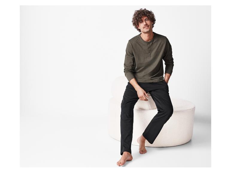 Man met krullend haar poseert in een donkergroene en zwarte pyjama.