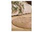 Beige bank met groene deken met bladeren en rond jute vloerkleed op houten vloer.