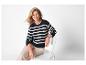 Femme souriante en pull rayé bleu marine et blanc, assise sur une chaise blanche.
