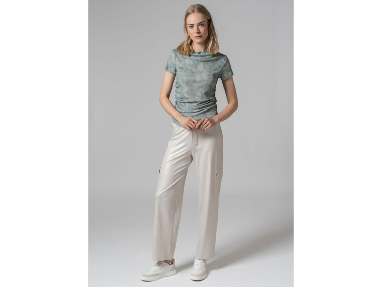 Een vrouw draagt een lichtblauw T-shirt met een patroon en beige broek.