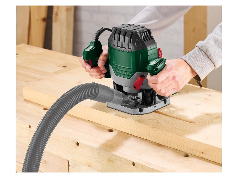 Persoon gebruikt een bovenfrees op een houten plank met aangesloten stofzuigerslang.