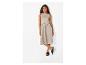 Vrouw in een mouwloze beige midi-jurk en zwarte sandalen, poserend tegen een witte achtergrond.