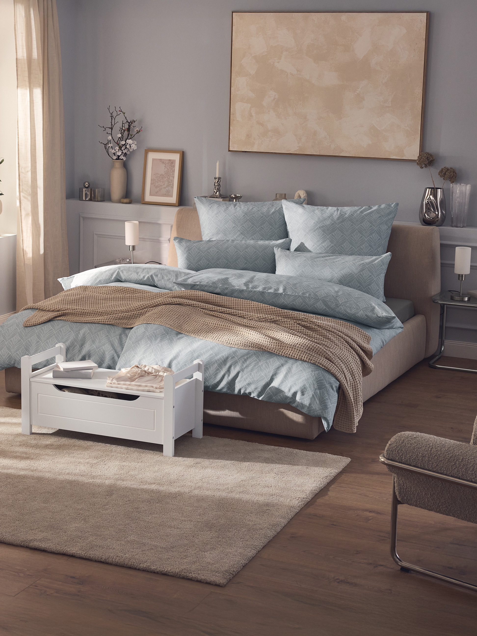 Moderne slaapkamer met tweepersoonsbed, blauw beddengoed met patroon, beige plaid en witte opbergkist.