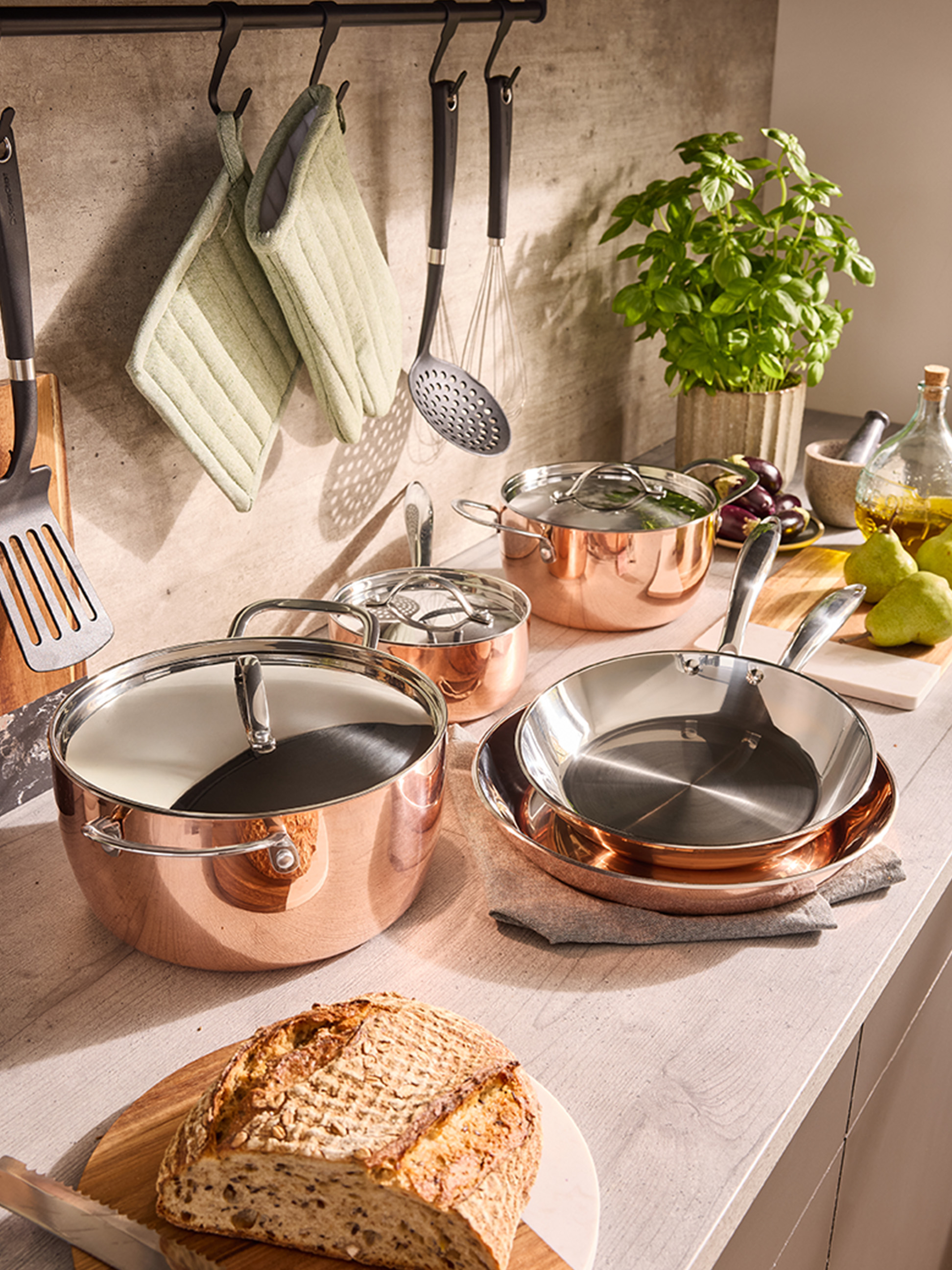Ensemble de casseroles et poêles en cuivre sur un comptoir de cuisine, avec du pain et des herbes.