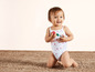 Een baby in een wit badpak met fruitprint, zittend op een jutekleed.