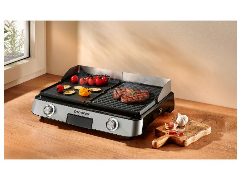 Elektrische grill met vlees en groenten, met knoflook en pepers ernaast.