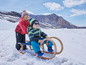 Twee kinderen in winterkleding op een houten slee in de sneeuw.