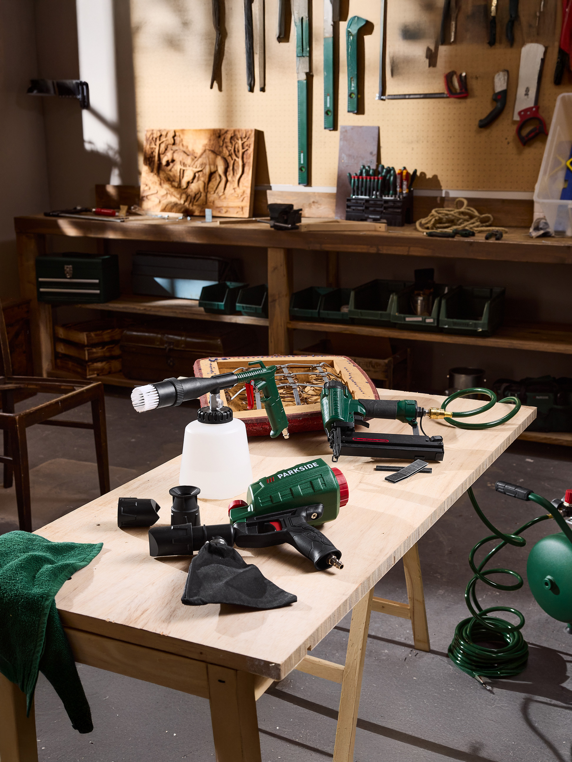 Outils pneumatiques Parkside, dont un cloueur et un pistolet pulvérisateur, sur une table en bois dans un atelier.