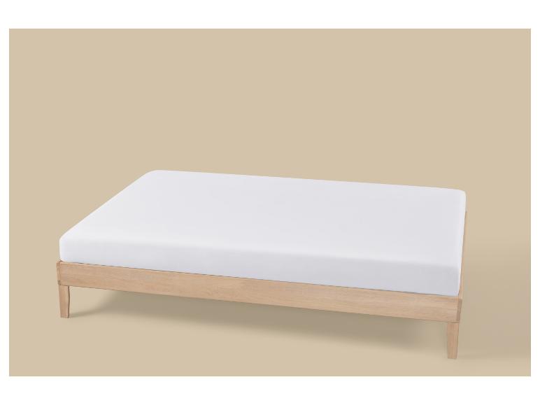 Een licht houten bedframe met een wit matras op een beige achtergrond.