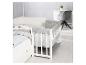 Lit bébé blanc avec literie grise et blanche, à côté d'un grand lit.