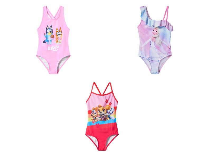 Trois maillots de bain pour filles: rose avec des chiens de dessin animé, bleu avec une princesse et rouge avec des chiots.
