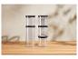Six récipients de rangement transparents avec couvercles noirs, empilés sur une table en bois.