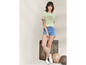 Een vrouw draagt ​​een lichtgroen US Grand Polo T-shirt en blauwe denim shorts.