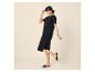 Femme souriante en robe noire ample et sandales noires.