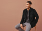 Man in een zwart corduroy jack en grijze broek.