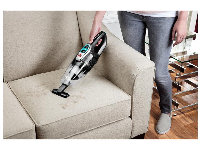 Vrouw reinigt stoffen bank met een Bissell kruimelzuiger