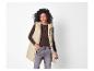 Vrouw in een beige lang vest, bruine top en grijze jeans.