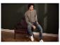 Man in bruin shirt met lange mouwen en blauwe jeans, zittend in een leren fauteuil.