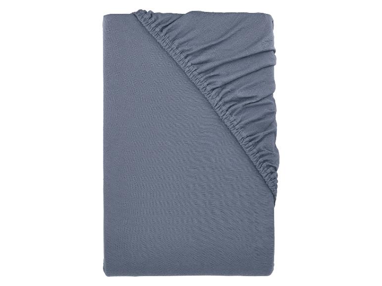 Drap-housse gris plié avec coins élastiqués.