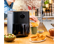 Vrouw pakt friet uit airfryer, met kip en spruitjes ernaast.